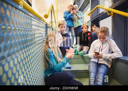 Studenti junior che usano smartphone a scuola Foto Stock