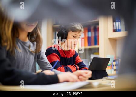 Ragazzo che indossa le cuffie mentre guarda il tablet digitale in classe Foto Stock