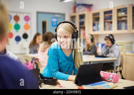 Sorridente ragazza che indossa le cuffie mentre usa il tavolo digitale in classe Foto Stock