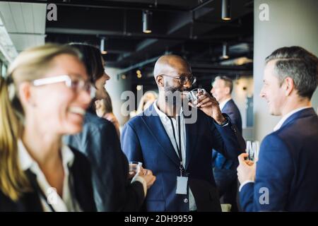 Un imprenditore sorridente che beve caffè nero mentre si trova in piedi con i colleghi ufficio Foto Stock