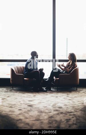 Colleghi di sesso femminile e maschile che discutono mentre si siedono contro la finestra a. luogo di lavoro Foto Stock