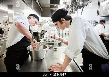 Vista laterale degli studenti di chef maschi che preparano cibo in commercio cucina Foto Stock