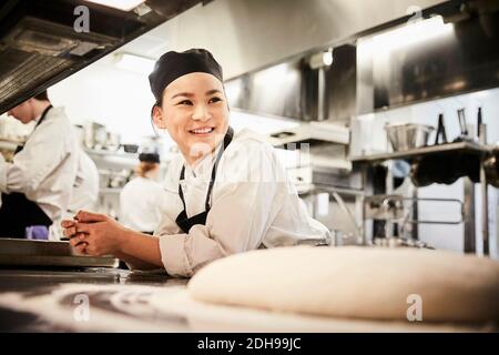 Sorridente chef femminile appoggiato al bancone in cucina commerciale Foto Stock