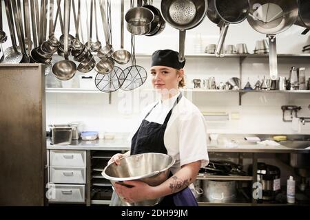 Ritratto di sicuro chef femmina che tiene contenitore in cucina commerciale Foto Stock