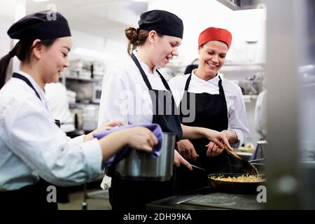 Insegnante che guarda le studentesse dello chef che cucinano cibo in cucina commerciale Foto Stock