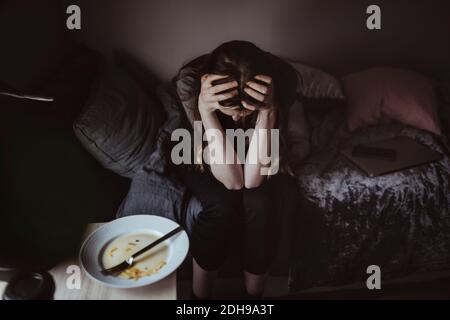 Vista ad alto angolo di una donna preoccupata seduta sul letto Foto Stock