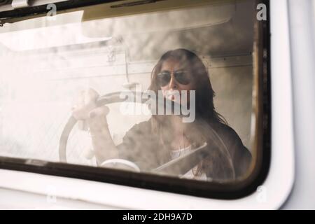 Donna d'affari che indossa occhiali da sole mentre guida un camion portatile per ufficio Foto Stock