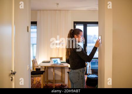 Ragazza adolescente che usa un tablet digitale montato a parete a casa Foto Stock