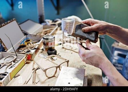 Immagine ritagliata del proprietario maschio che sfrega gli occhiali con l'attrezzatura in officina Foto Stock