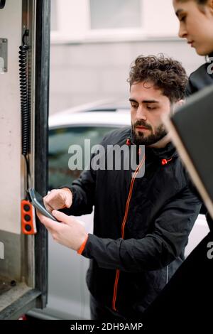 Giovane uomo di consegna che mostra il telefono cellulare alla collega di sesso femminile da carrello Foto Stock