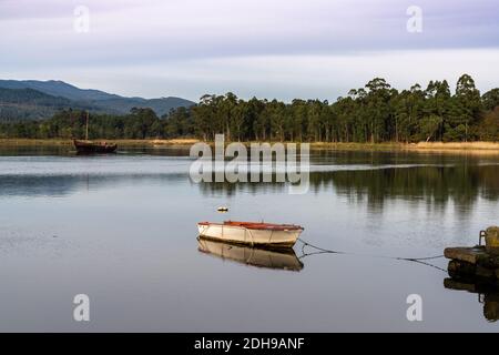 Due barche ancorate su un tranquillo e tranquillo fiume con colline e montagne e foreste dietro Foto Stock