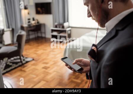 Visualizzazione ad alto angolo della messaggistica di testo di un uomo d'affari tramite telefono cellulare in camera d'albergo Foto Stock