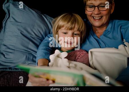Nonna sorridente che legge il libro di storia per il nipote sul letto a. casa Foto Stock