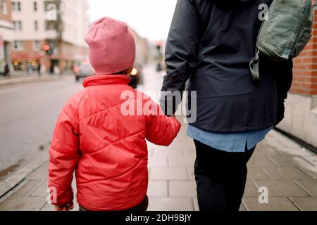 Vista posteriore del nipote che tiene la mano della nonna mentre cammina sul sentiero in città Foto Stock