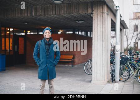 Ritratto di uomo felice che indossa in piedi contro l'edificio nel campus Foto Stock