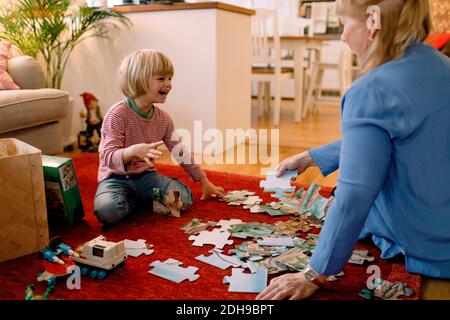 Ragazzo allegro che gioca puzzle con nonna in soggiorno Foto Stock