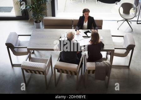 Vista ad alto angolo di avvocato femminile e clienti seduti a. scrivania in ufficio Foto Stock