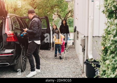 Uomo che carica l'auto elettrica mentre la famiglia carica i bagagli Foto Stock