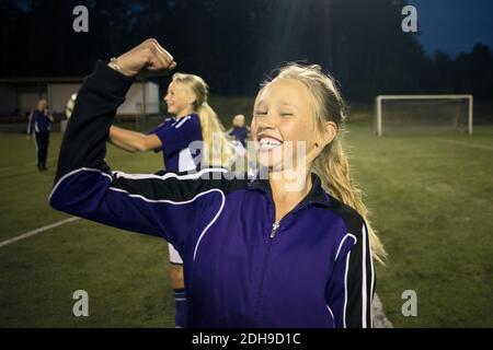 Ritratto di ragazza allegra che flette i muscoli contro gli amici sul calcio campo Foto Stock