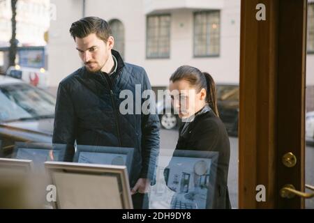 Giovane coppia che guarda le cornici delle immagini sul display viste da finestra office Foto Stock