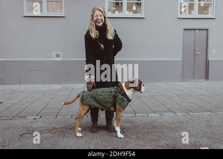 Giovane donna allegra in piedi con pugile contro la costruzione in città Foto Stock