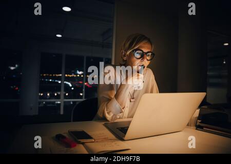 Donna d'affari premurosa che guarda il notebook mentre lavora tardi nella creatività ufficio Foto Stock