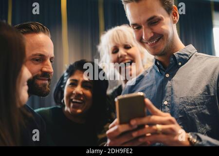 Felice gente di affari che usa lo smartphone con collega maschio dentro ufficio Foto Stock