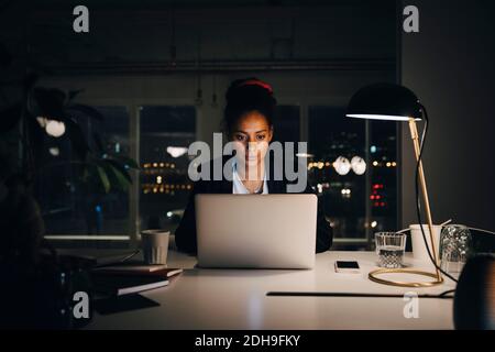 Giovane donna d'affari dedicata che lavora tardi mentre usa il computer portatile alla creatività ufficio Foto Stock