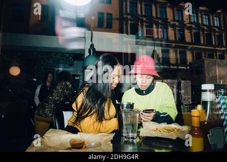 Uomo che mostra smartphone a donna sorridente visto attraverso trasparente finestra in vetro Foto Stock