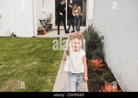 Ritratto di ragazza che mostra bacchetta magica con la famiglia in background in cantiere Foto Stock