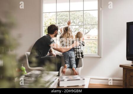 Padre con figlie che guardano attraverso la finestra a casa Foto Stock