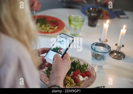 Immagine ritagliata di donna che fotografa il cibo attraverso smartphone a. tavolo da pranzo Foto Stock