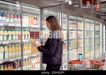 Vista laterale della donna che tiene bottiglie di succo nella sezione refrigerata nel supermercato Foto Stock