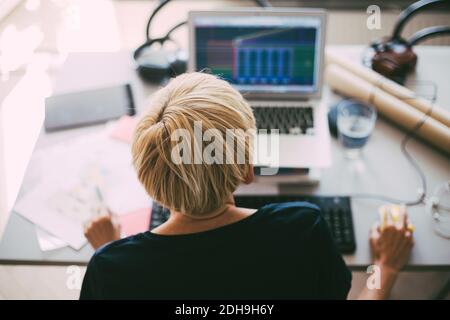 Vista posteriore di una donna che lavora con un computer portatile in ufficio a. casa Foto Stock