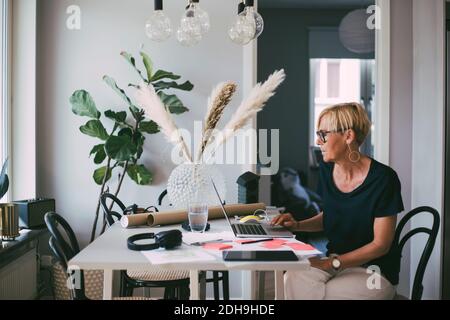 Donna che lavora a casa seduta al tavolo di lettura sul computer portatile schermo Foto Stock