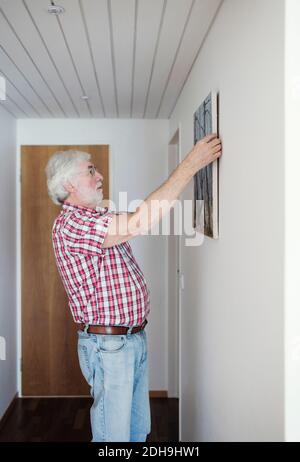 Vista laterale della pittura a sospensione uomo anziano su parete bianca a casa Foto Stock