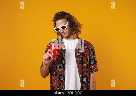 Immagine di un giovane uomo focalizzato in occhiali 3d in posa con coppa di plastica isolata su sfondo giallo Foto Stock