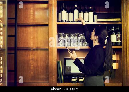 Vista laterale del proprietario che controlla l'elenco delle bottiglie di vino mentre in piedi nel cafe Foto Stock
