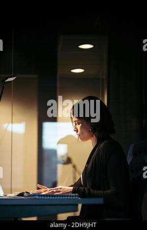 Vista del profilo di una donna d'affari seria che lavora alla scrivania al buio ufficio Foto Stock