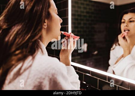 Donna mid adulta che guarda nello specchio mentre applica il rossetto a. hotel Foto Stock