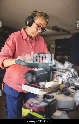 Donna anziana con sega circolare in officina Foto Stock