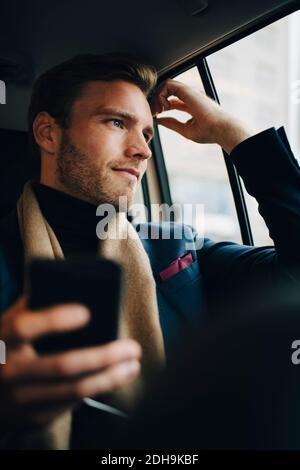 Uomo d'affari sicuro in vestito guardando attraverso la finestra mentre si siede dentro taxi Foto Stock