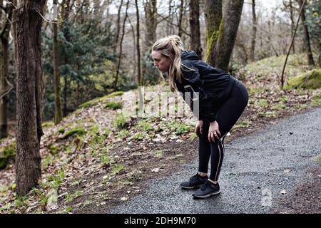 Tutta la lunghezza dell'atleta stanca in piedi con le mani ginocchia nella foresta Foto Stock