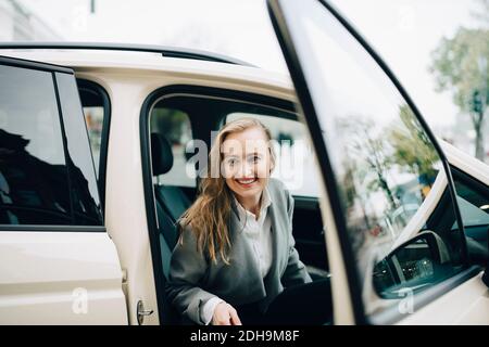 Sorridente imprenditore che esce dal taxi durante il viaggio d'affari Foto Stock