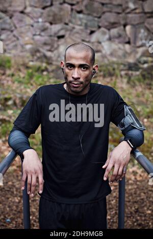 Ritratto di un atleta maschile sicuro che pende su barre parallele foresta Foto Stock