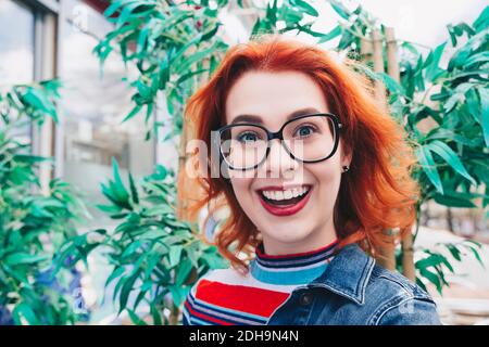 Ritratto di giovane donna sorridente rosso contro pianta Foto Stock