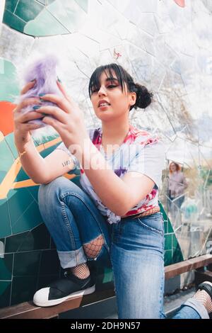 Giovane donna che usa il telefono cellulare dalla parete del mosaico Foto Stock