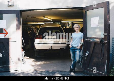 Ritratto di donna sicura appoggiata sulla porta all'ingresso di officina di riparazione automatica Foto Stock