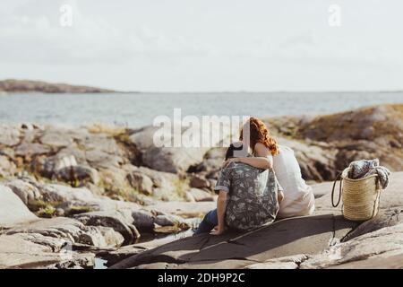 Vista posteriore dell'incollaggio di madre e figlio mentre si è seduti sopra terreno roccioso durante il giorno di sole Foto Stock