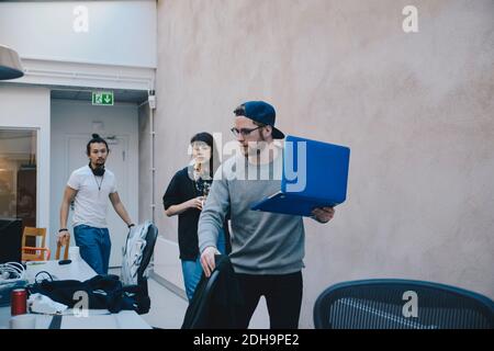 Programmatore di computer che tiene un computer portatile mentre si cammina con i colleghi in ufficio Foto Stock